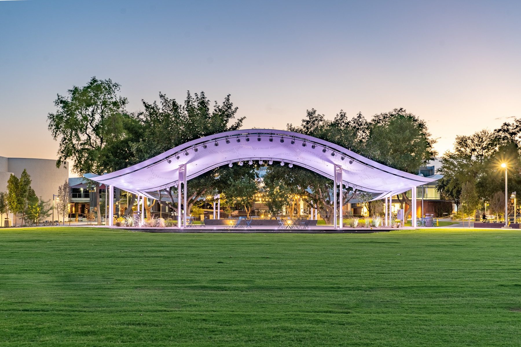 A lit performance canopy over a lawn at blue hour