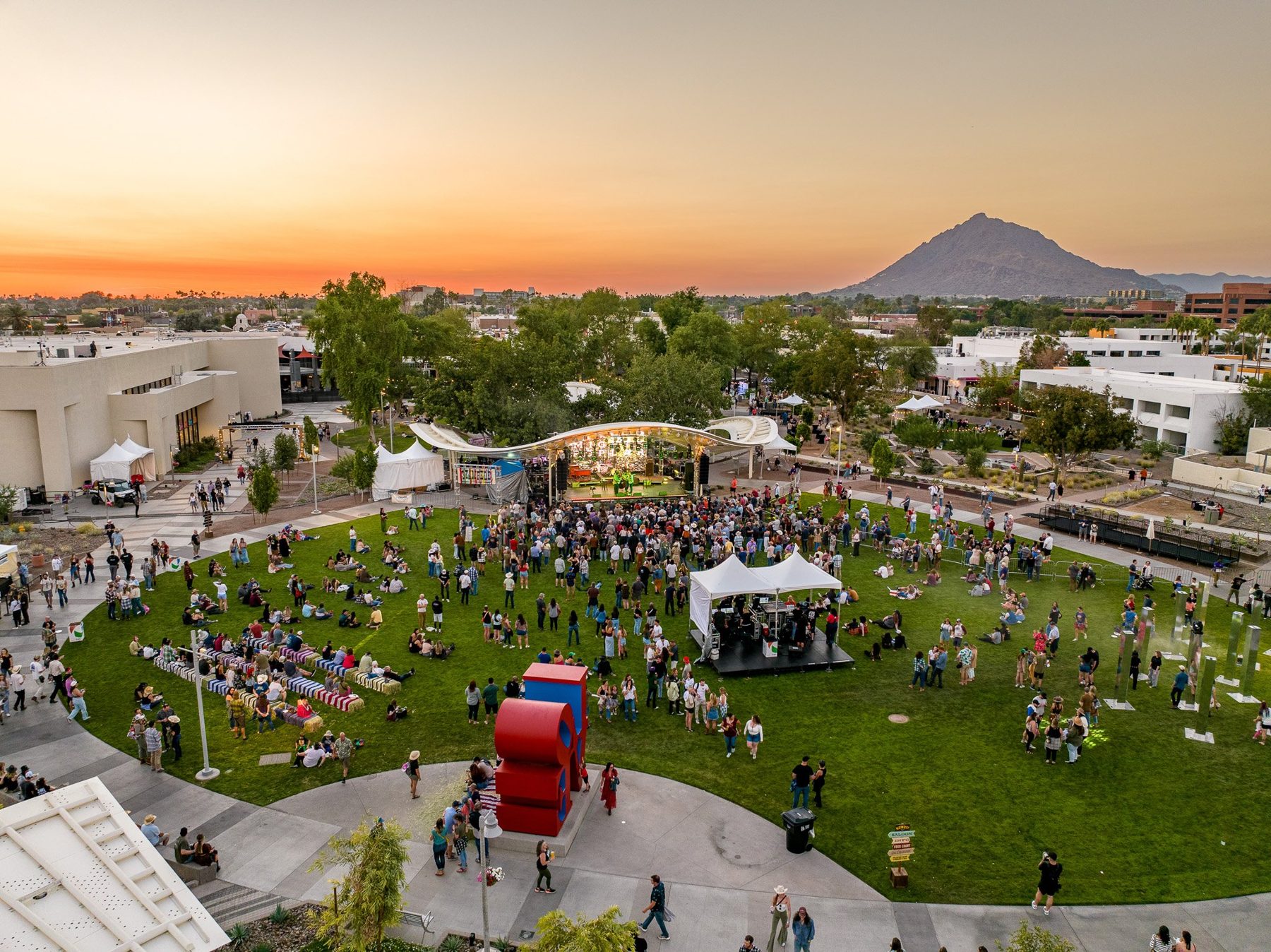 A festival crowd on a park lawn at sunset, from the air