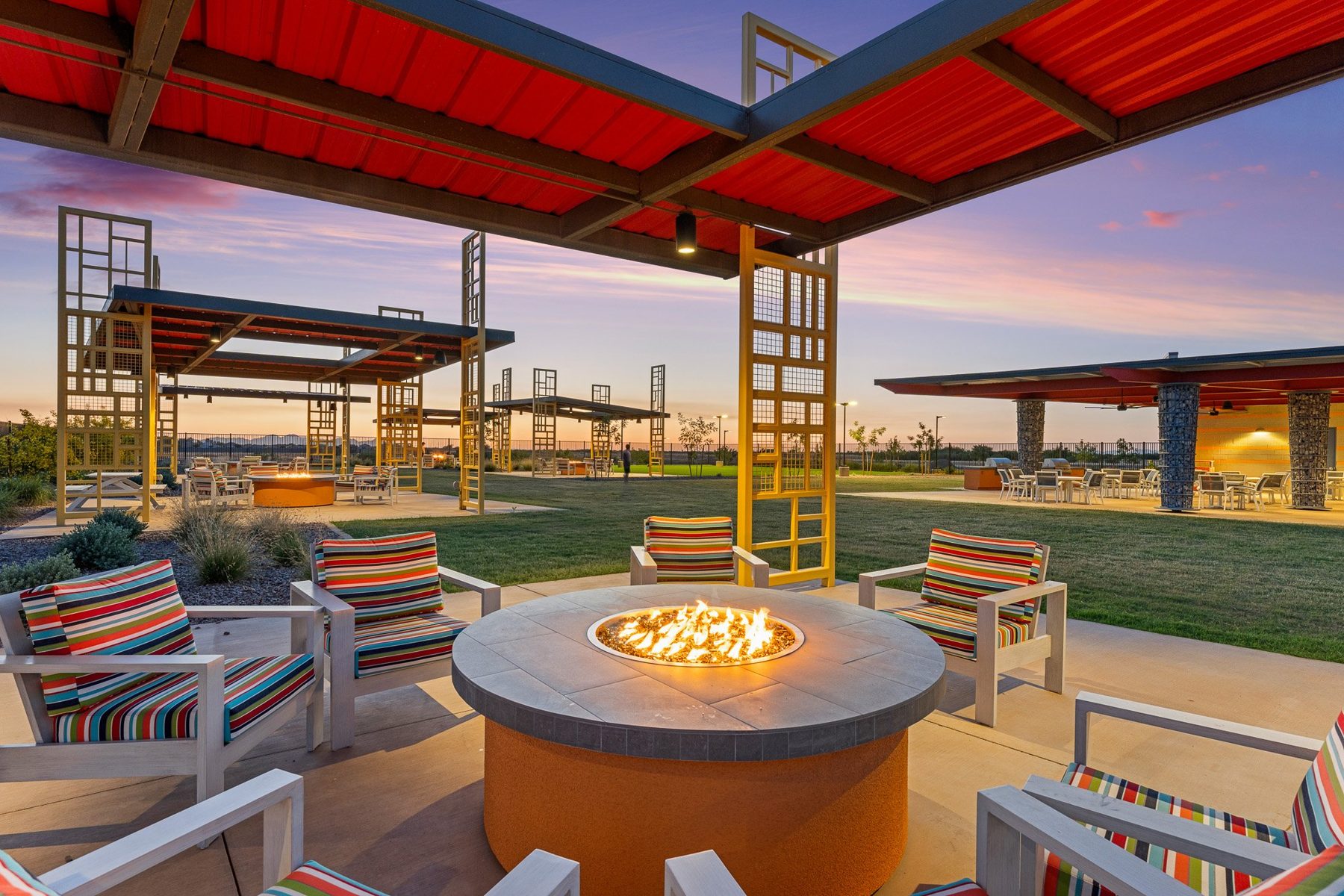 A fire pit lounge under a red shade canopy at blue hour