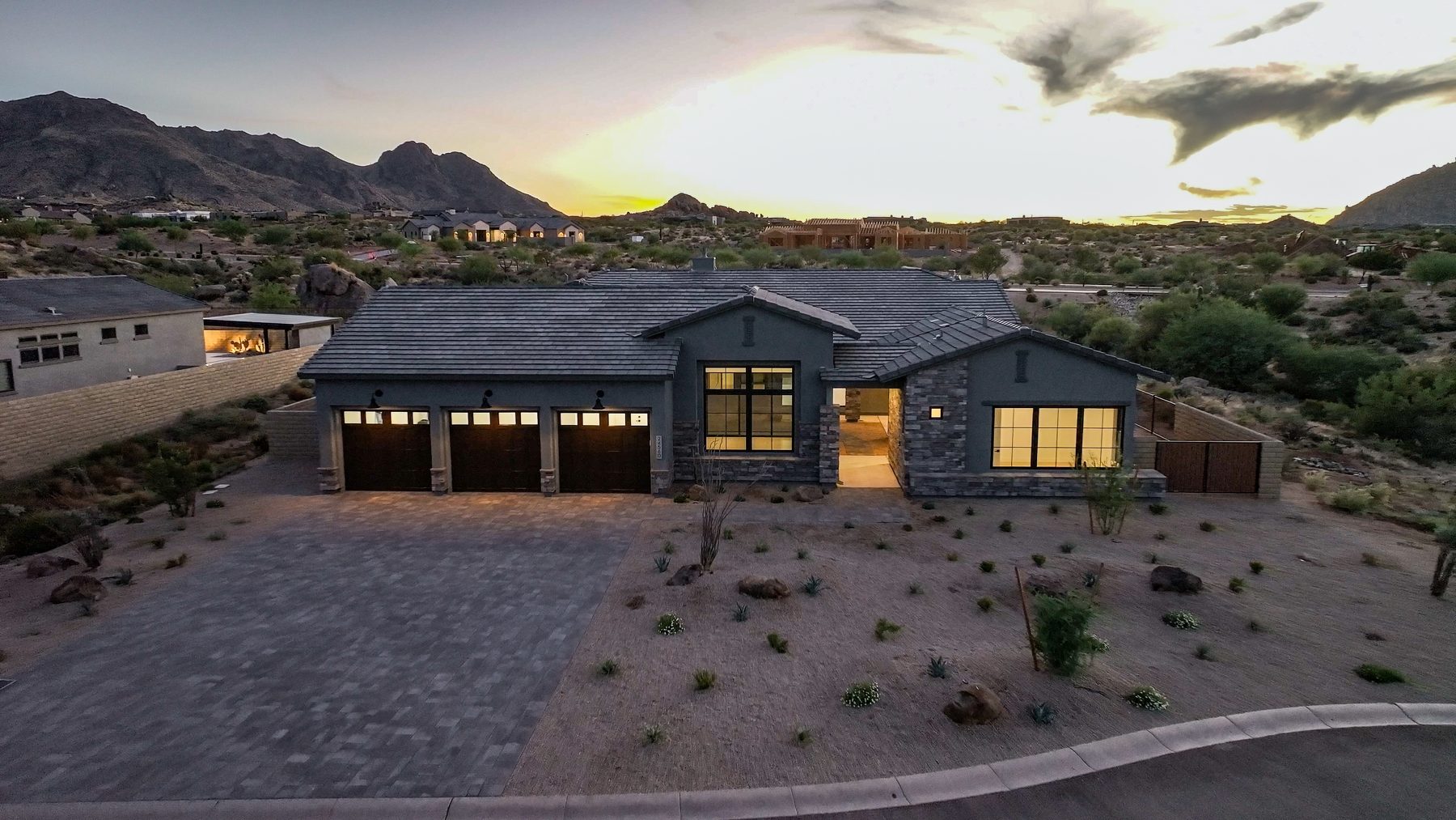 A home at twilight with its windows lit and mountains behind